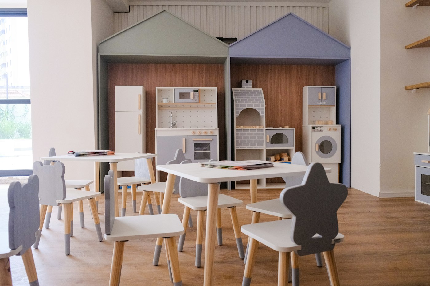 A bright Montessori classroom with small wooden tables, star-shaped chairs and a play kitchen